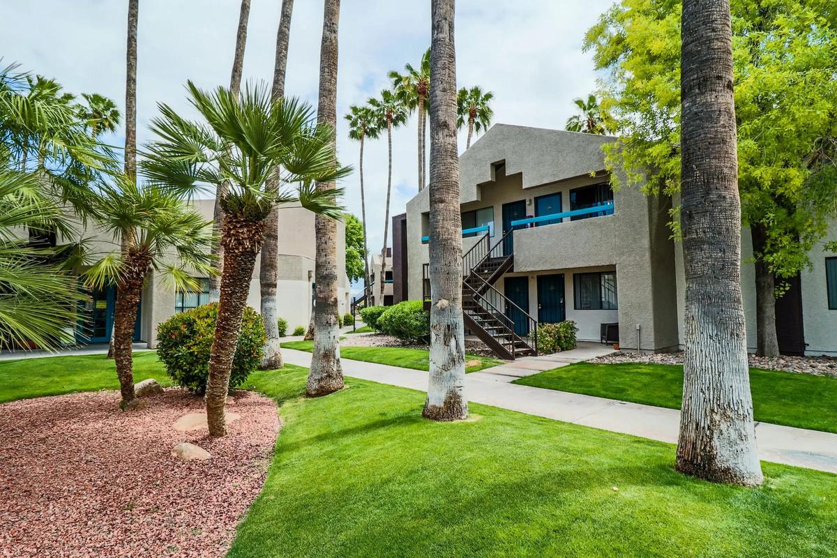 Two-storey building with exterior stair, green lawn and palm trees, daytime