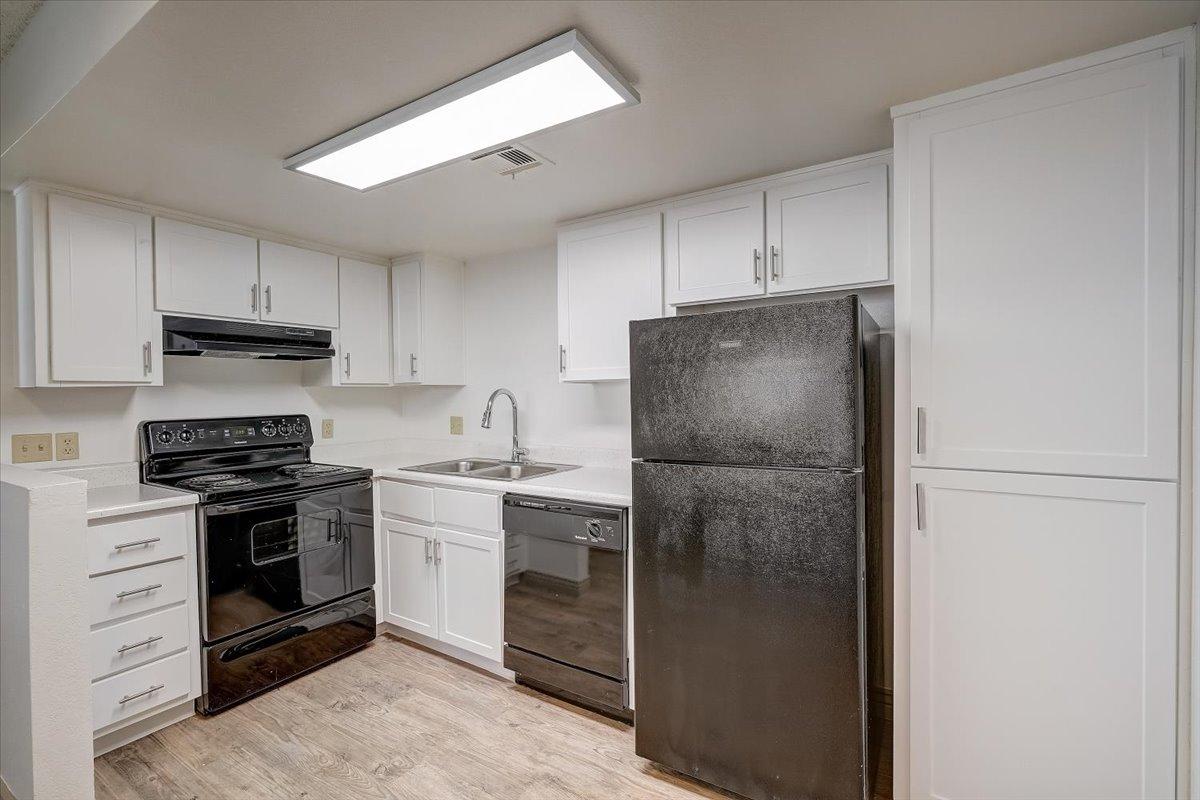 Vacant kitchen: white cabinets, black range, dishwasher and refrigerator