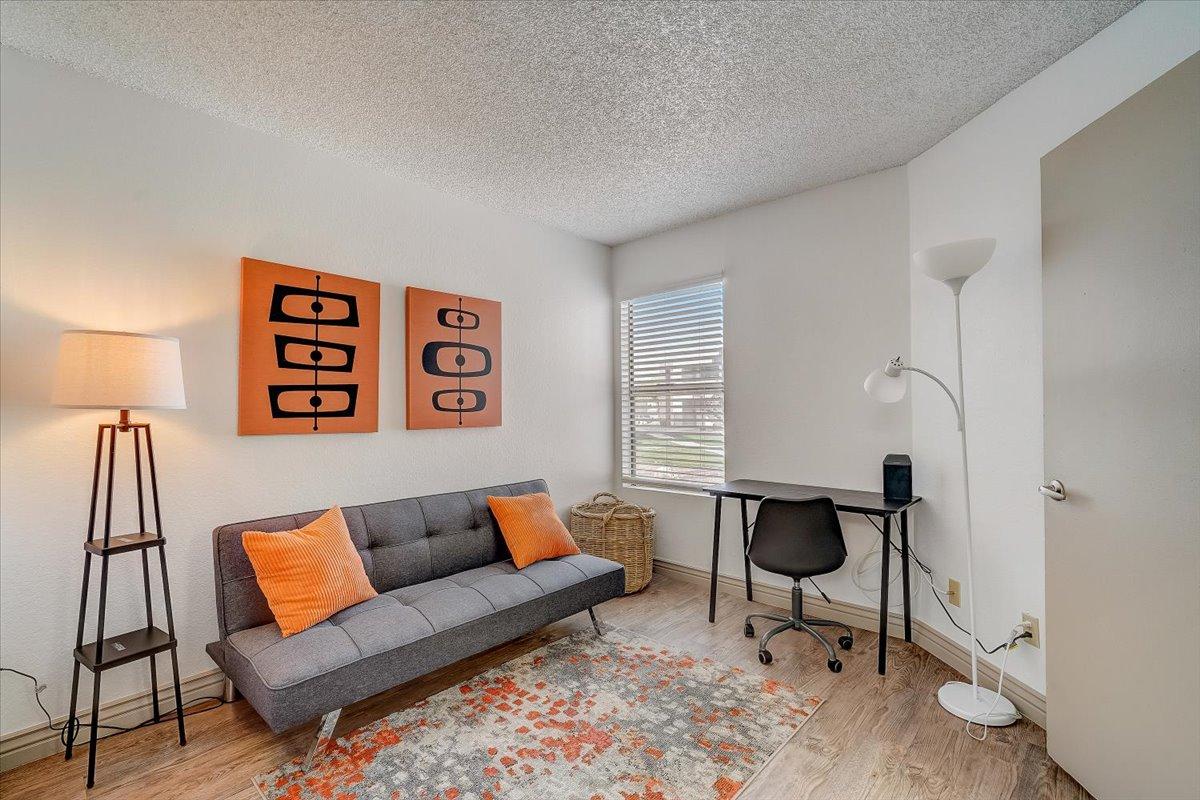 Second bedroom furnished as an office: grey futon, orange pillows, desk and chair