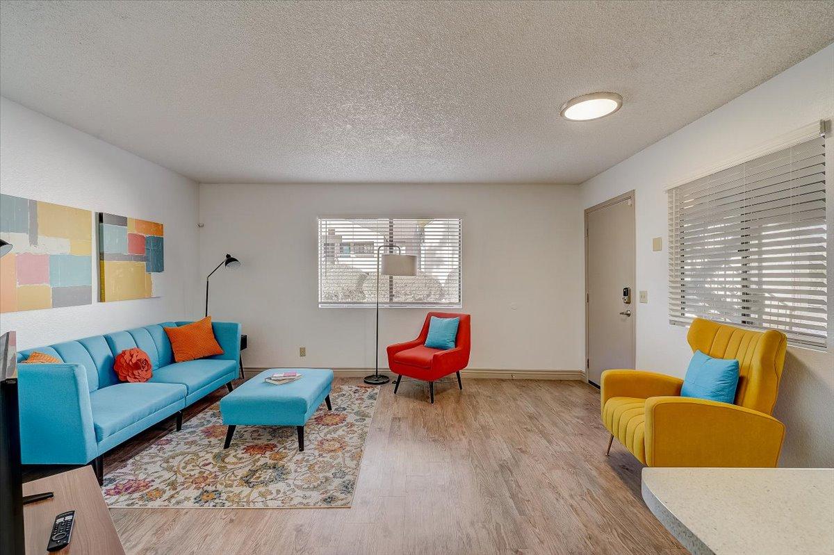 Furnished living room: blue sofa, red and yellow armchairs, patterned rug, wood-look vinyl floor