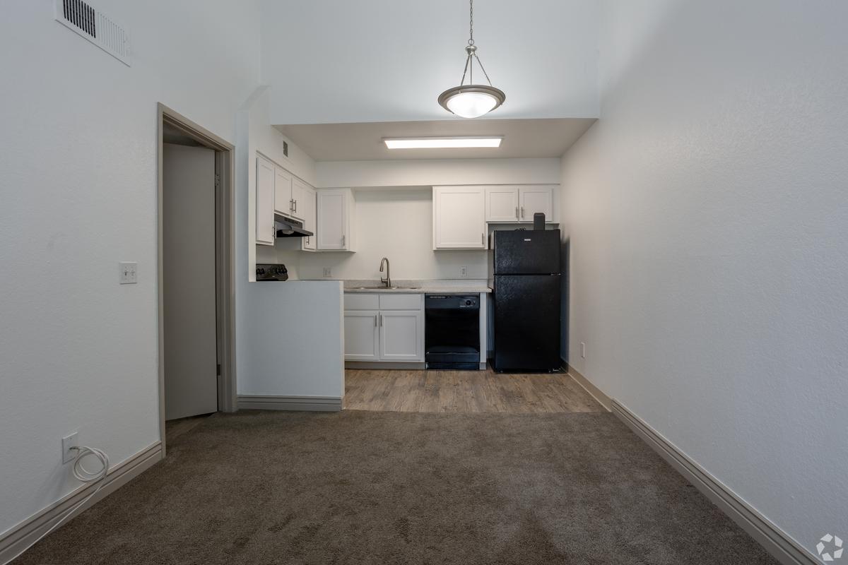 Vacant kitchen and carpeted living area, white cabinets, black refrigerator