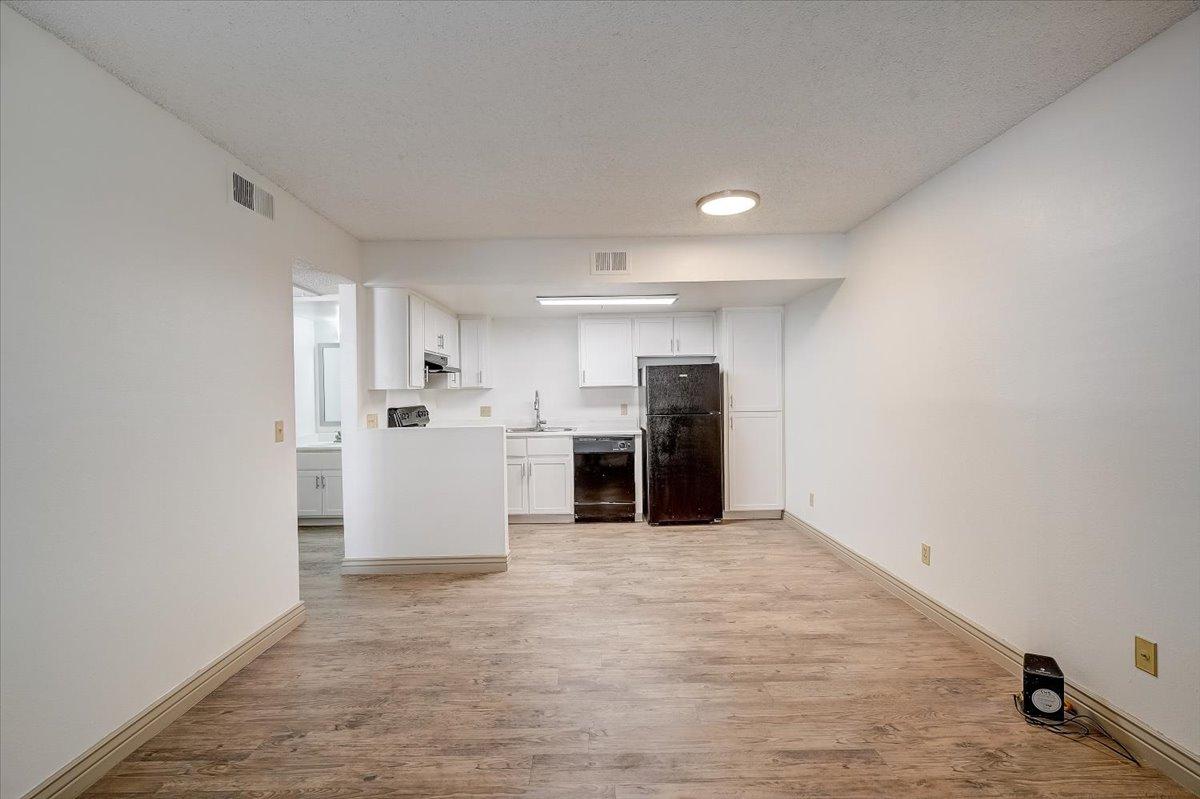 Vacant living room with kitchen beyond, wood-look vinyl floor