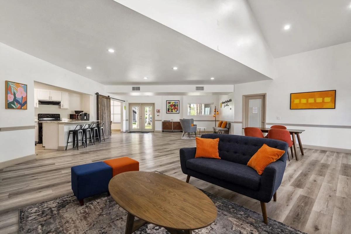 Clubhouse lounge: navy sofa with orange pillows, round coffee table, kitchen and bar seating behind