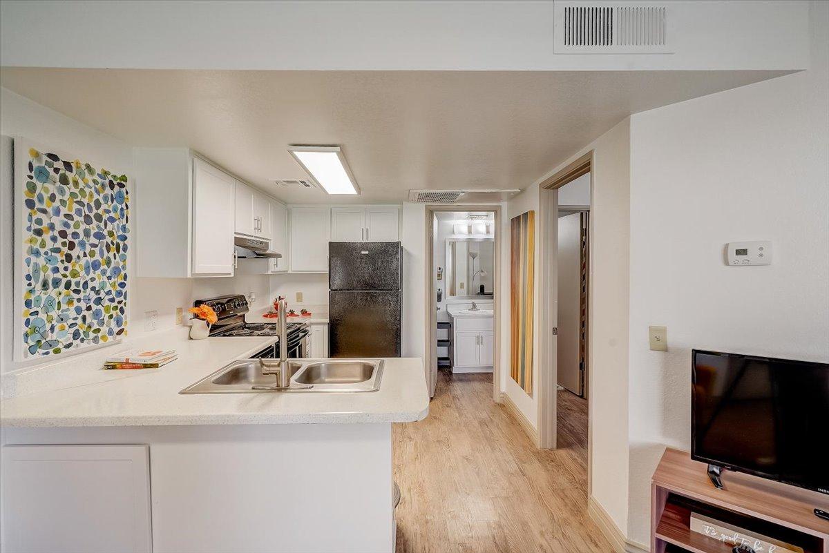Kitchen with white shaker cabinets, black appliances and the living room beyond